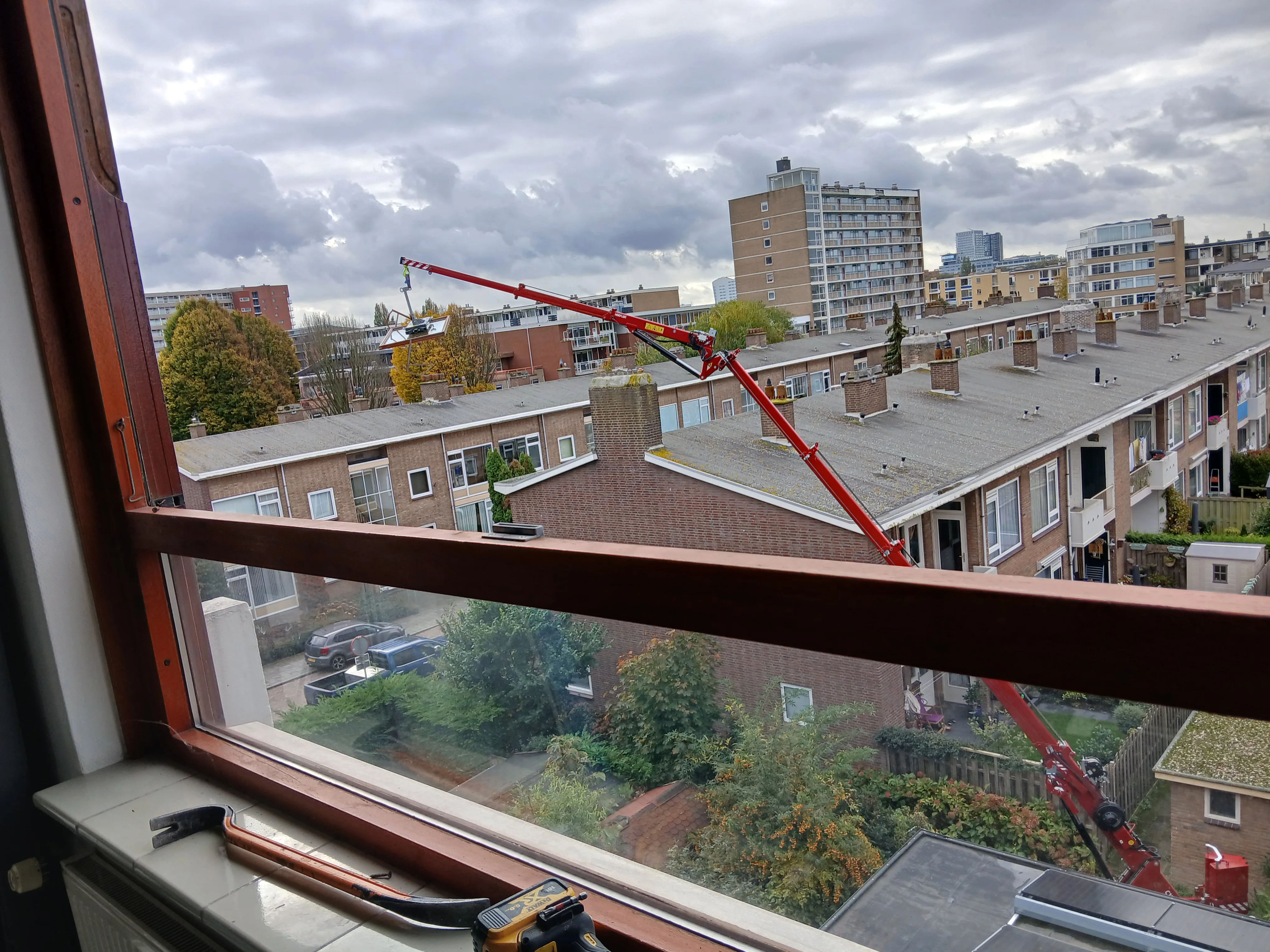 Uitzicht op een stad met een open raam en een kraan die kozijnen plaatst