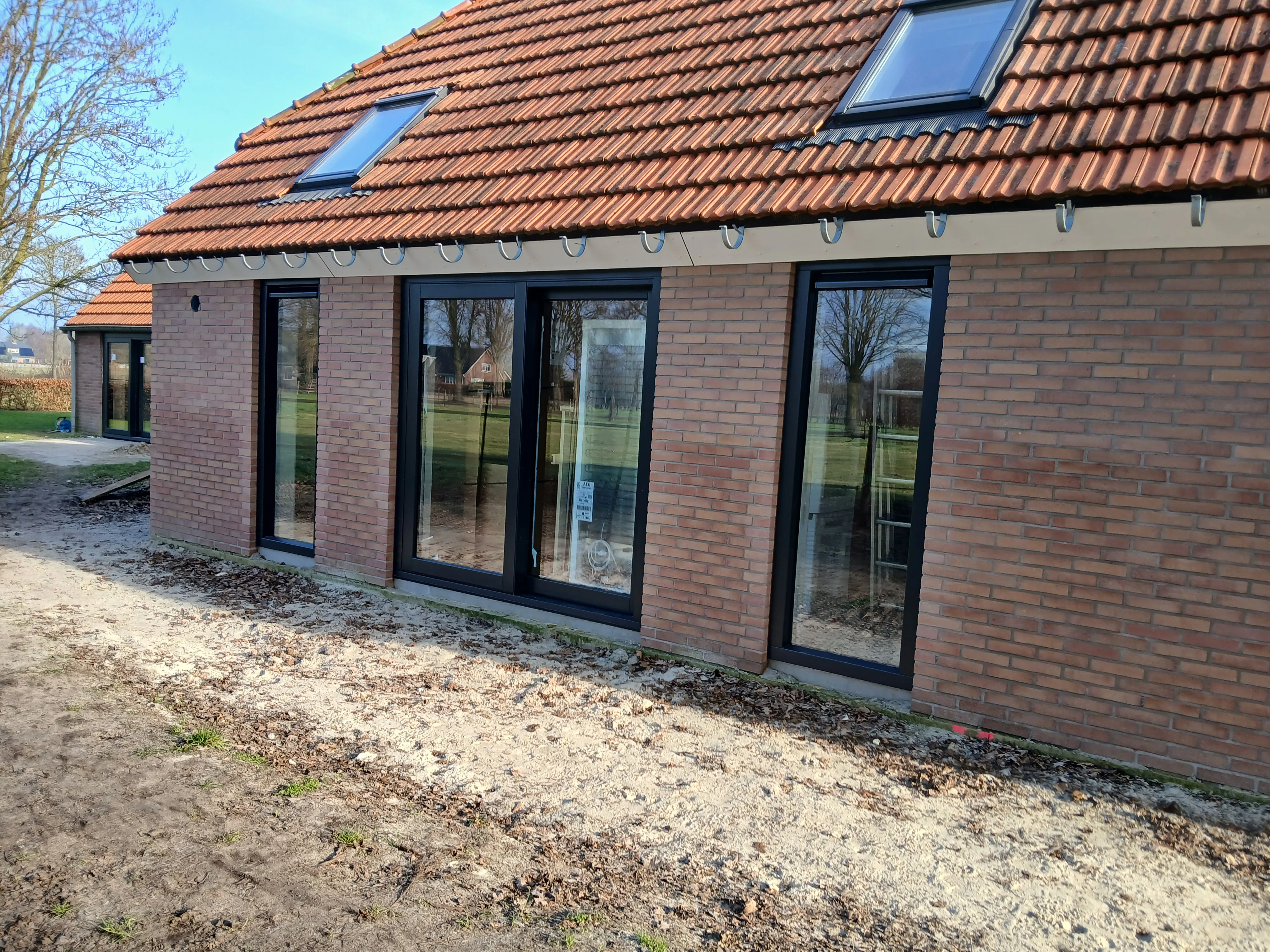 Een moderne woning met aluminium schuifpuien en dakramen, omgeven door een tuin