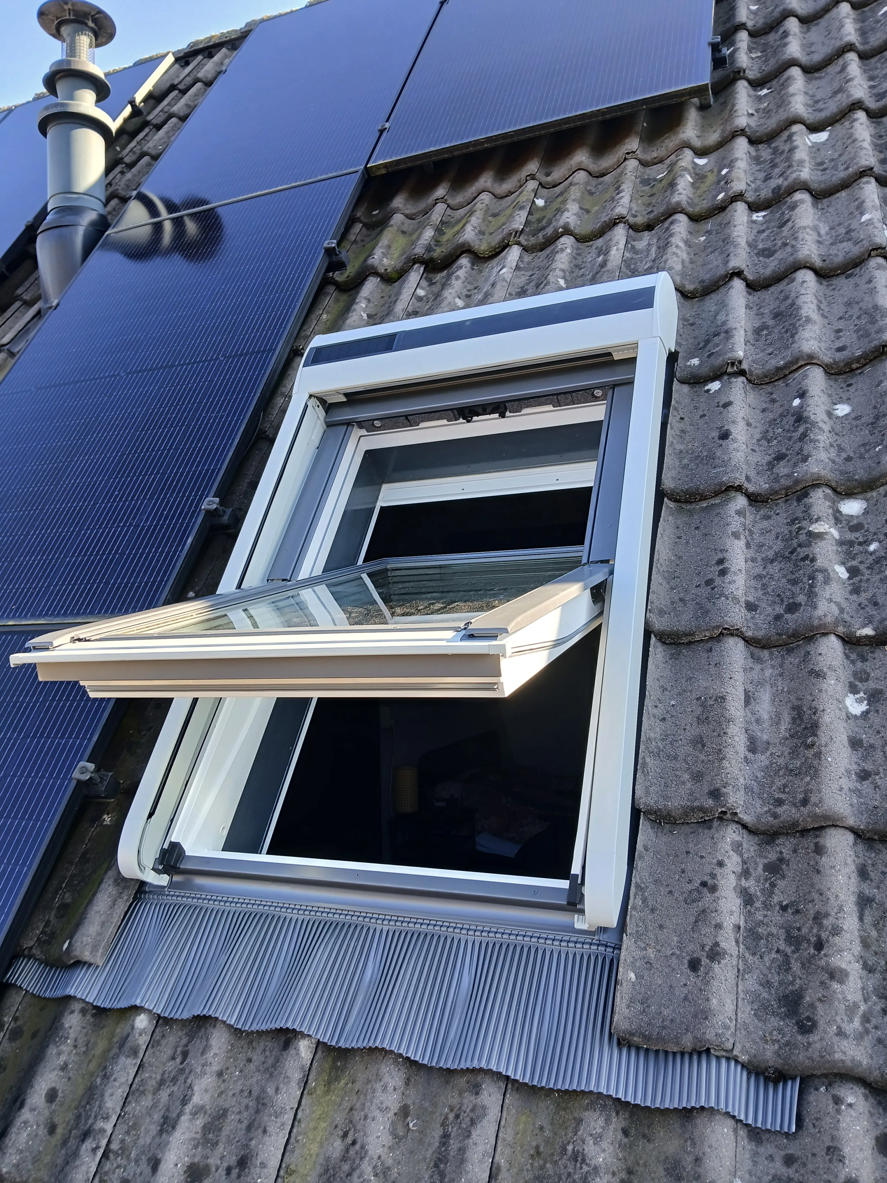 Dakraam met geopend venster, geplaatst op een hellend dak met zonnepanelen ernaast
