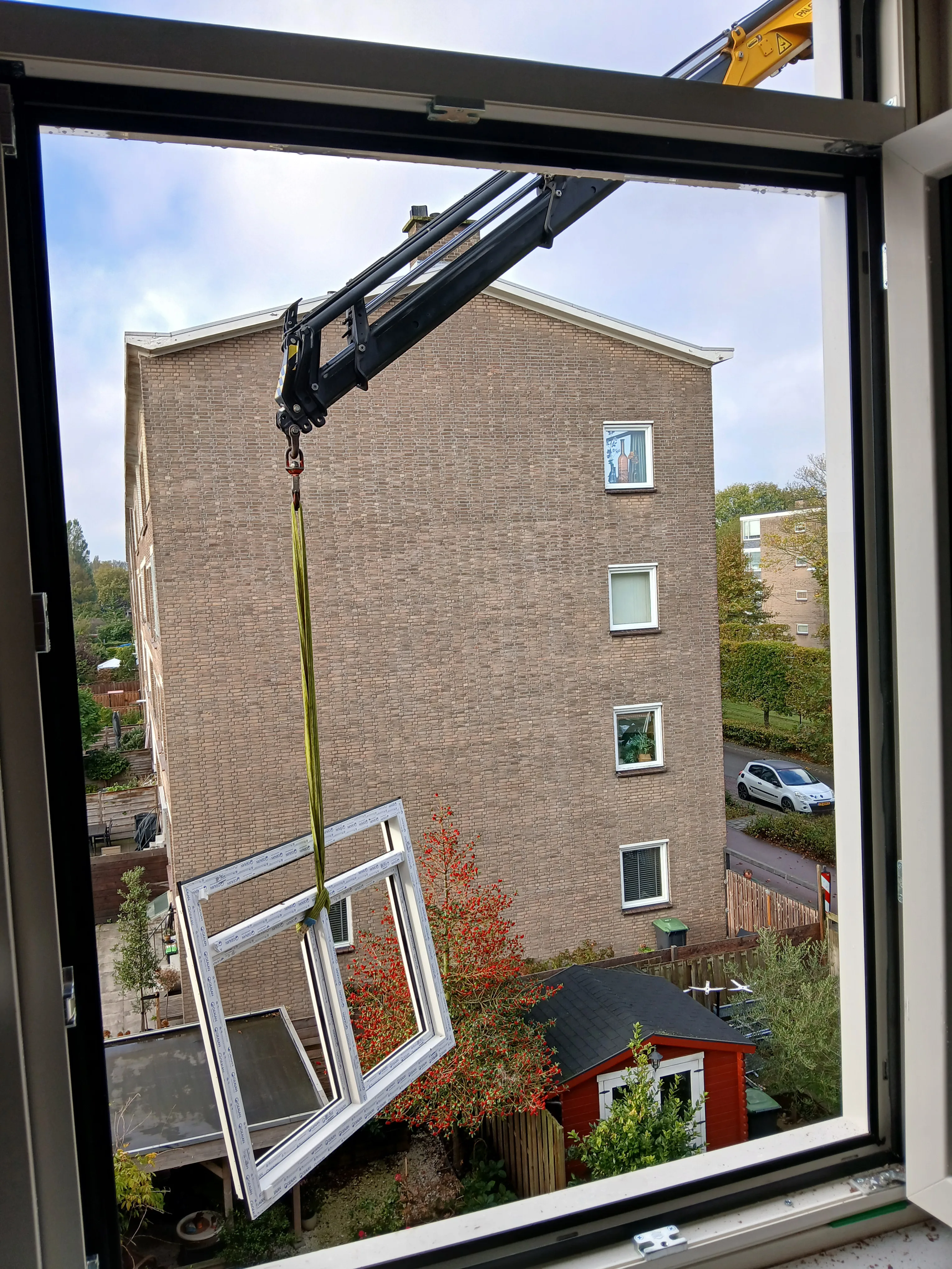 Een kunststof kozijn wordt vervangen door een kraan in een woongebied met een appartementencomplex