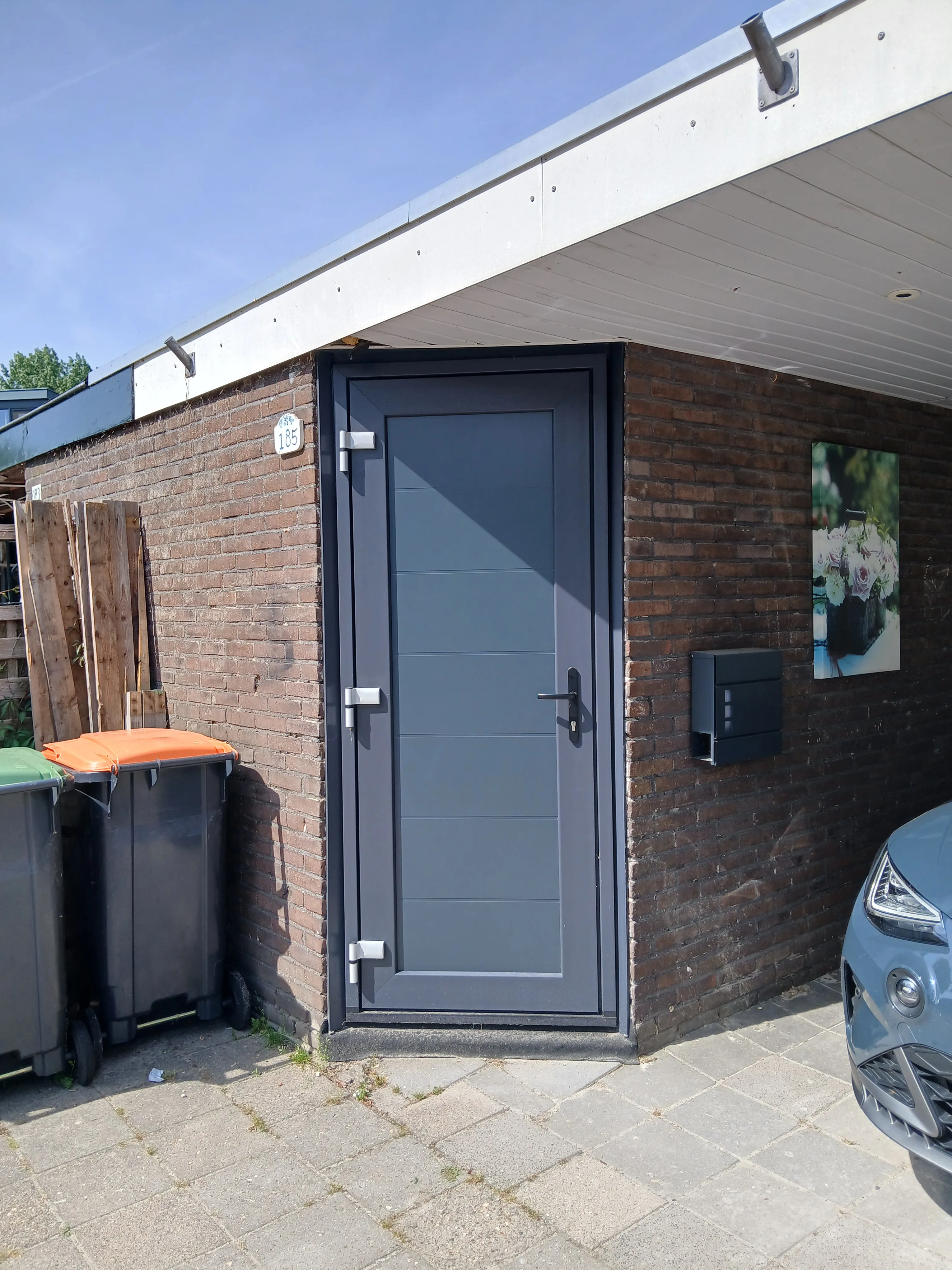 Moderne kunststof voordeur met een strakke afwerking en een bruin stenen muur erachter