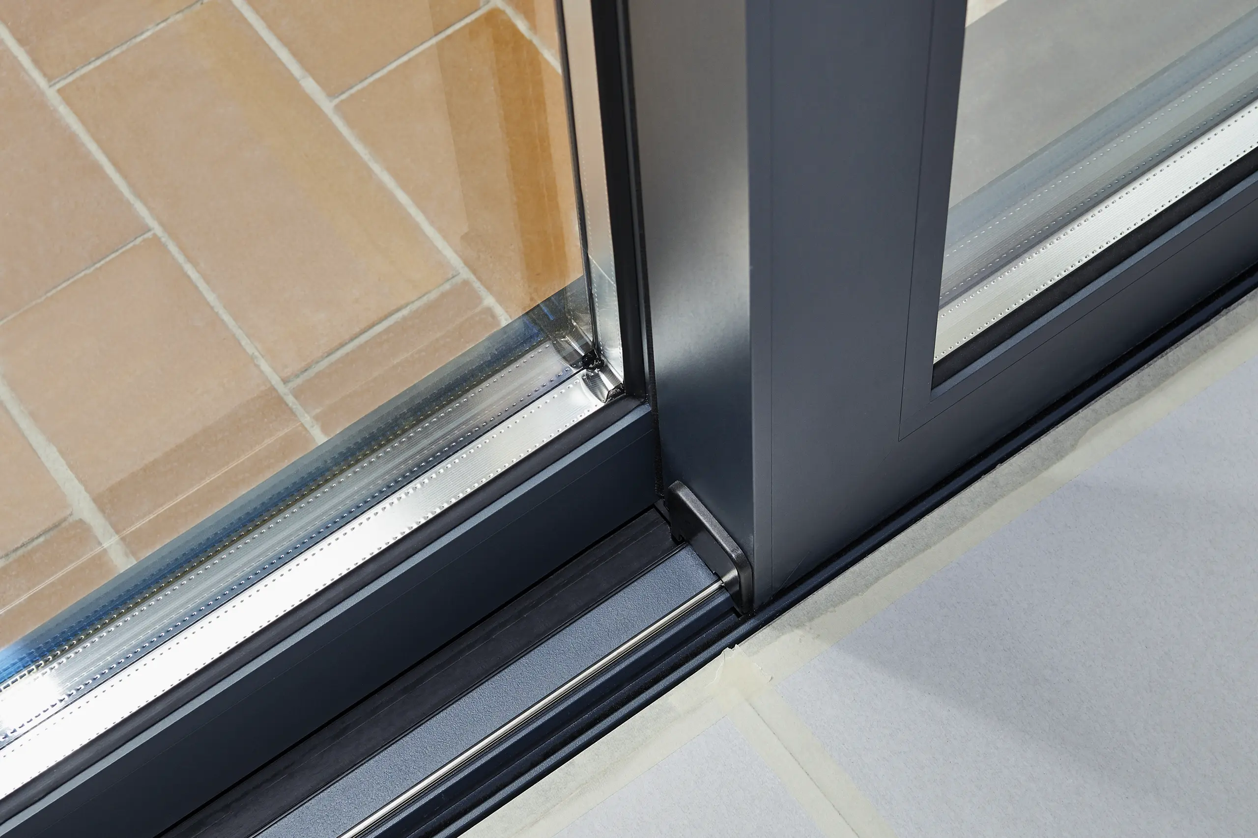 Detail van een aluminium schuifpui met moderne afwerking en tegels op de vloer